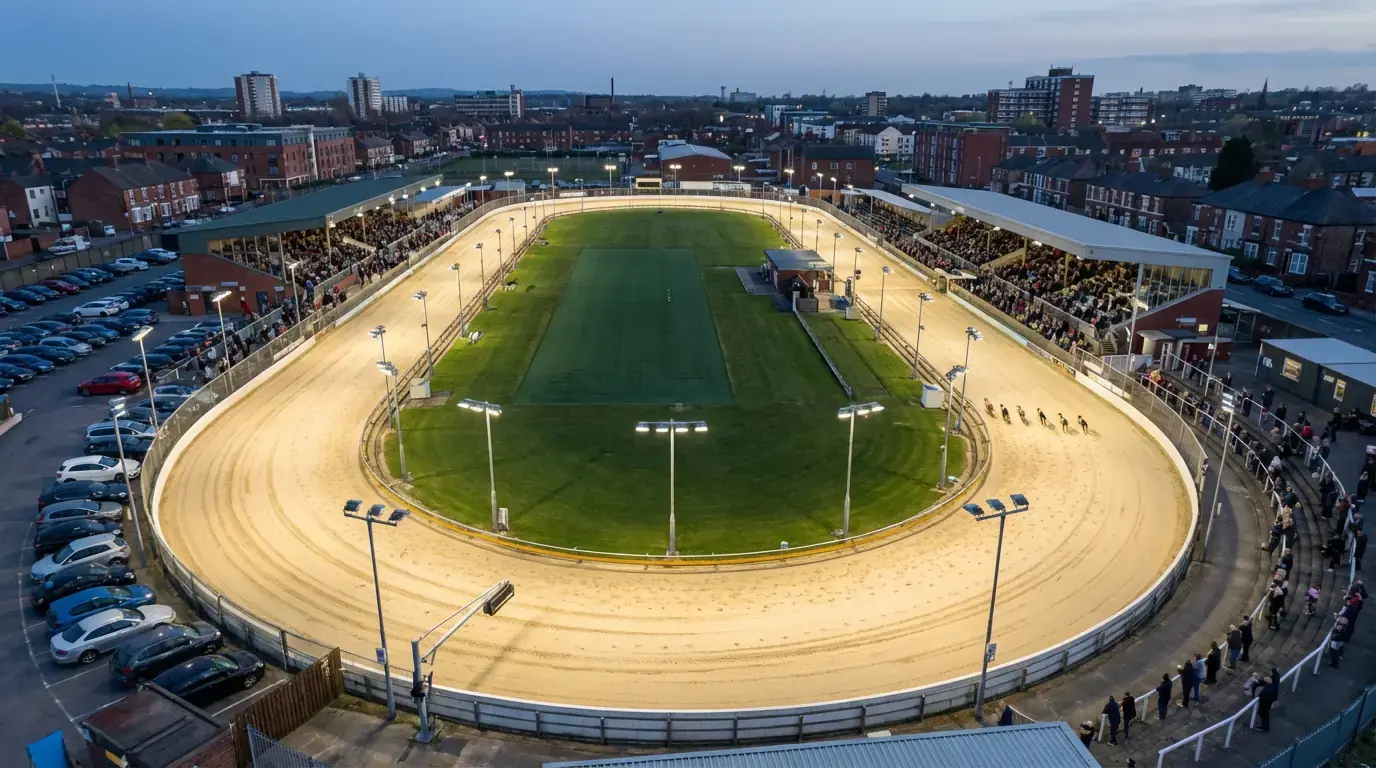 Aerial view of an illuminated UK greyhound racing stadium during an evening meeting